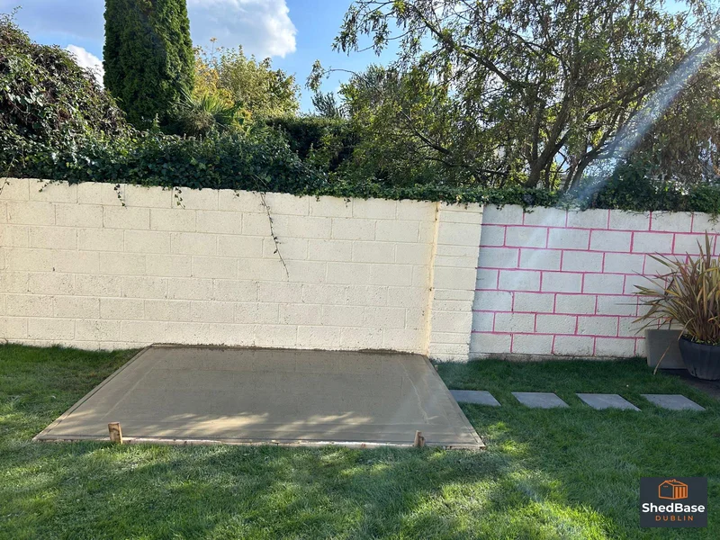 Concrete shed base beside a garden wall, with stepping stones across the lawn