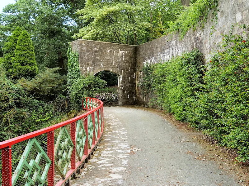 Terrace path under a stone arch at Mount Congreve, with a red and green railing